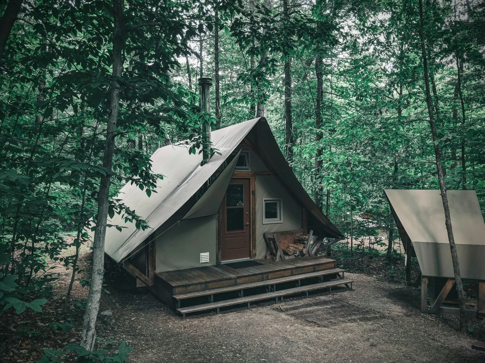 A peaceful A-frame tent cabin nestled in a lush Canadian forest, perfect for rustic camping.
